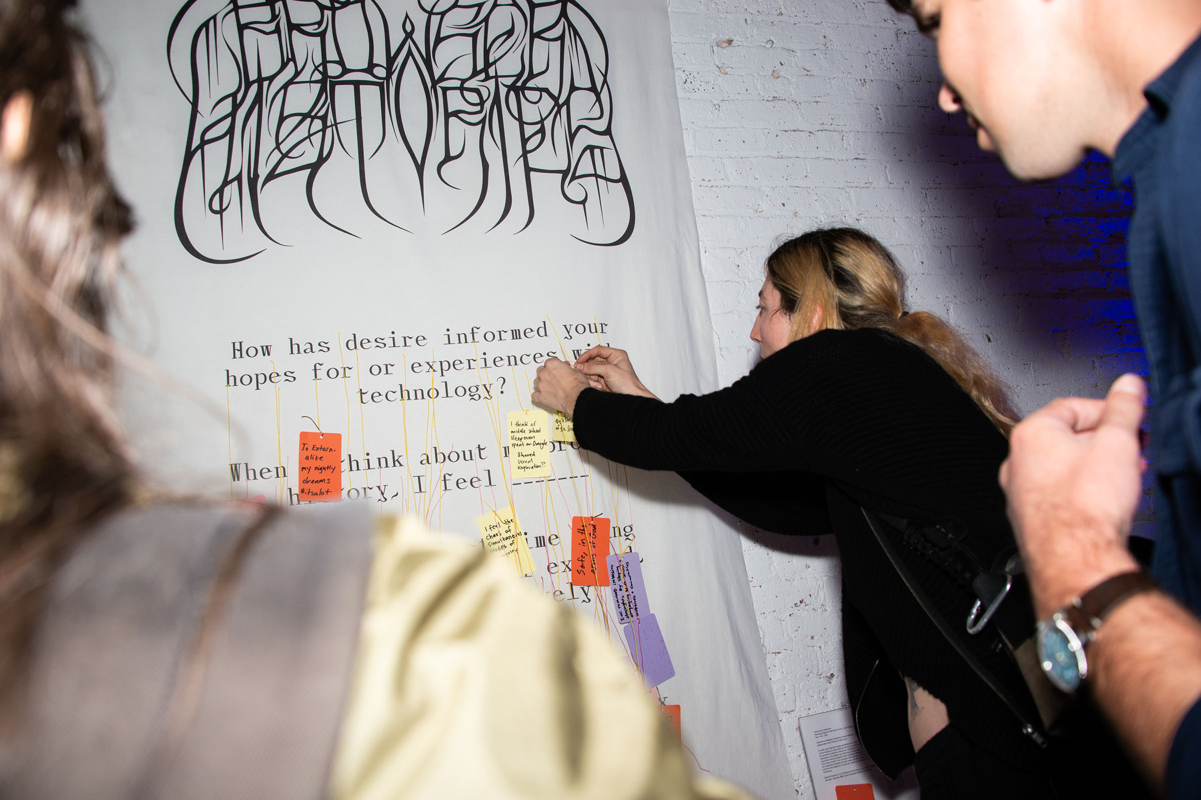 A group of people gather around the banner, and one person ties a card to the dangling strings.