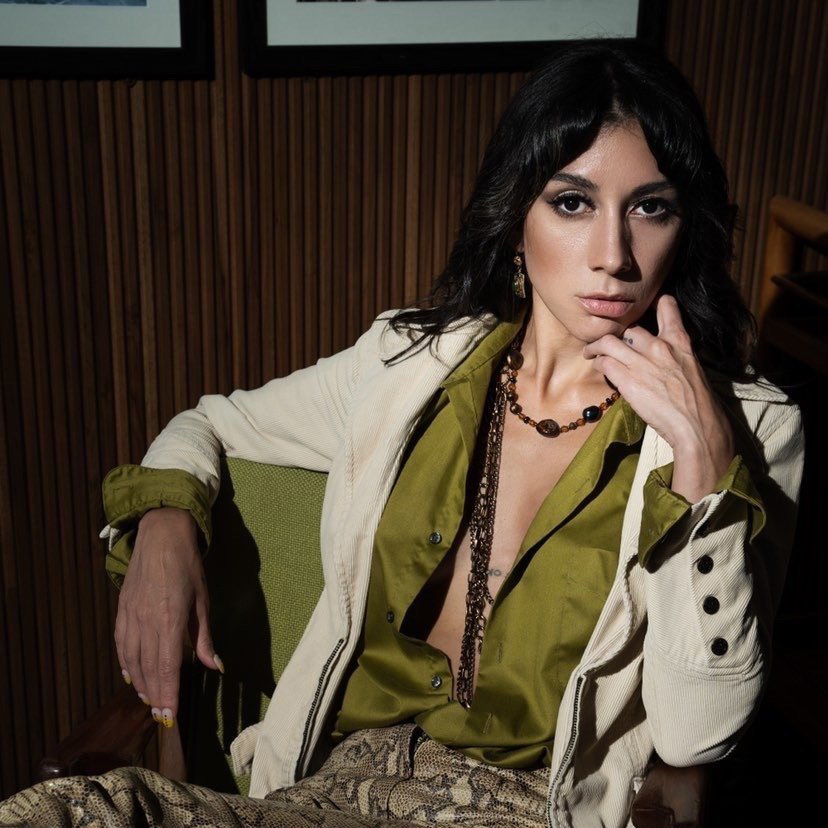 A photo of Gabriella Garcia shows a woman in a green satin shirt open to the waist, tucked into snakeskin pants, and topped with an off-white jacket.